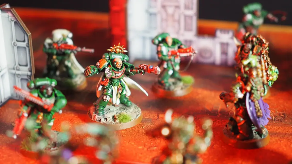 Space Marines und Plague Marines stehen sich auf einem roten Schlachtfeld voller Trümmer gegenüber