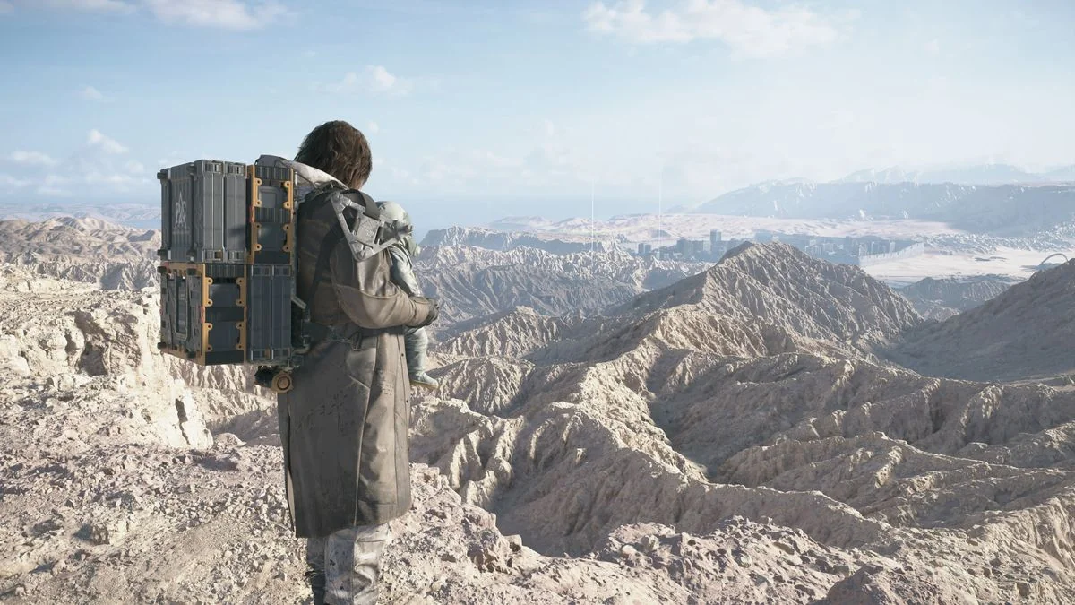 Death Stranding 2 Geburtstag DOOMS: Sam, mit Lou auf seiner Brust, steht auf einem Berg und blickt über ein Wüstental.