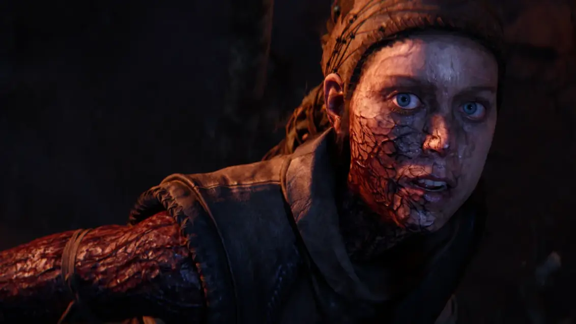 Senua blickt in die Kamera, während die dunkle Fäulnis sichtbar ihren Arm hinauf in ihr Gesicht kriecht.